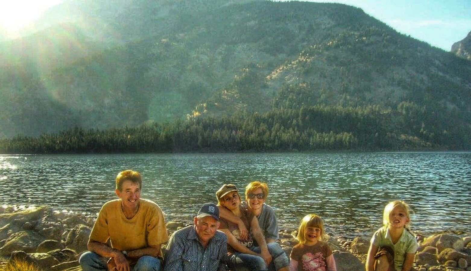 Family sitting together on rocky shores of an alpine lake with mountain backdrop