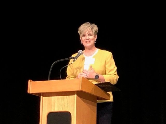 Woman speaking at podium in yellow blazer at a conference